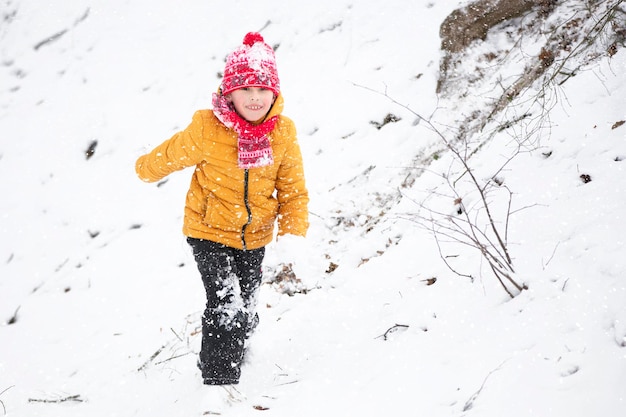 Zabawny mały chłopiec w kolorowych ubraniach bawiący się na świeżym powietrzu podczas opadów śniegu
