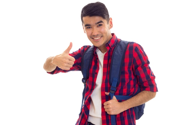 Zabawny młody człowiek z czarnymi włosami w białej koszulce i czerwonej koszuli w kratkę z niebieskim plecakiem