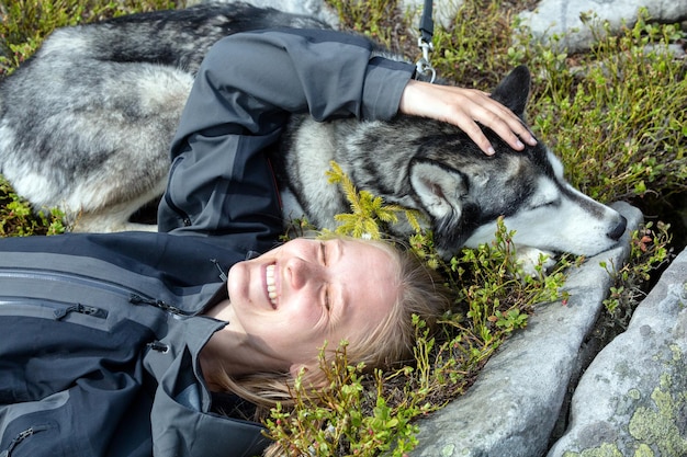 Zabawny portret pięknego psa husky syberyjskiego śpiącego i uśmiechniętej turystki na tle zielonej trawy scenariusz wędrówki na świeżym powietrzu