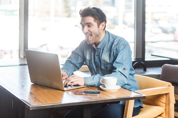Zabawny, pozytywny człowiek freelancer pracujący na laptopie z rozmową wideo pokazującą język