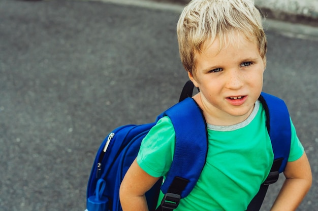 Zabawny psotny śliczny blond chłopiec z piegami niebieski plecak ze szkoły lub przedszkola artystyczne emocje wyraz twarzy mikro chwile proste radości szczęśliwe dzieciństwo edukacja problemy psychologia