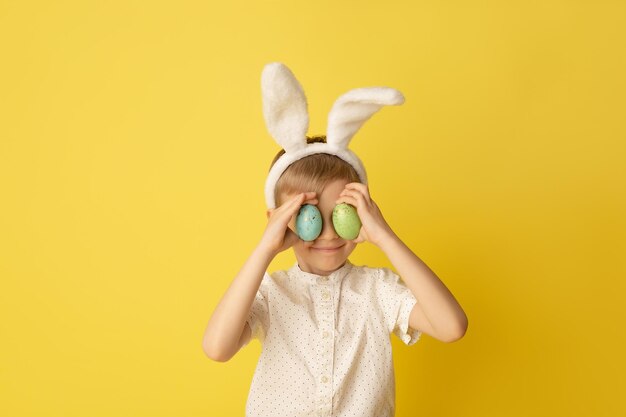 Zabawny szczęśliwy chłopiec dziecko z pisanki i uszy królika na żółtym tle