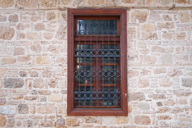 Zabytkowe okno z drewnianymi ramami i czarną kratką na kamiennej zabytkowej ścianie budynku