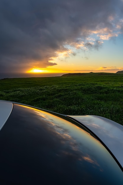 Zachód słońca na horyzoncie ze złotymi chmurami i refleksami na szybie samochodu na pierwszym planie