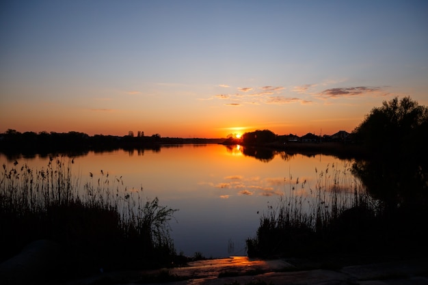 Zachód słońca nad jeziorem, słońce zachodzi za drzewami i piękne refleksy w wodzie
