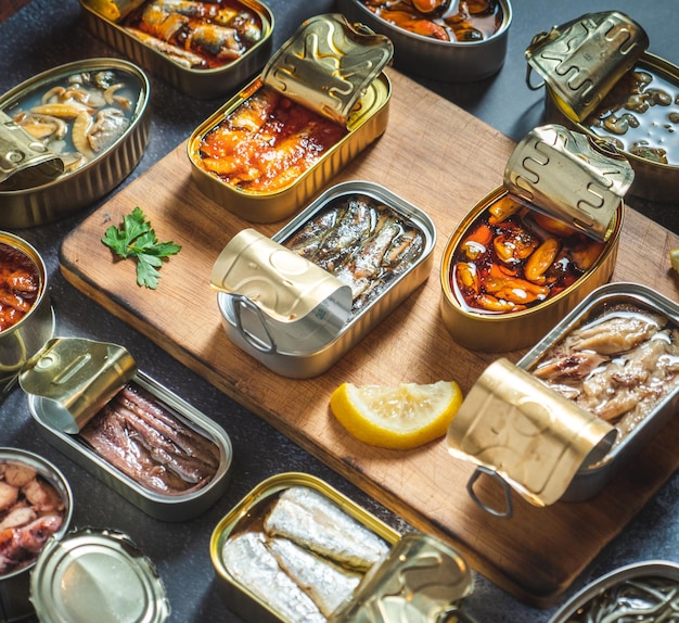 Zdjęcie zachowaj puszki z różnymi produktami z ryb i owoców morza otwarte na ciemnym stole
