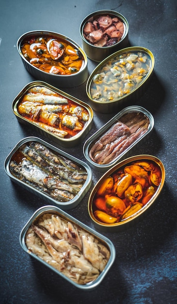 Zdjęcie zachowaj puszki z różnymi produktami z ryb i owoców morza otwarte na ciemnym stole