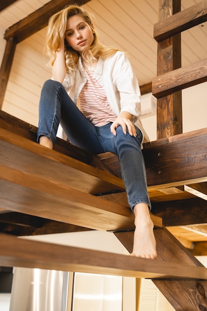 Zachwycona dziewczyna patrząca prosto w kamerę, siedząca na drewnianych schodach