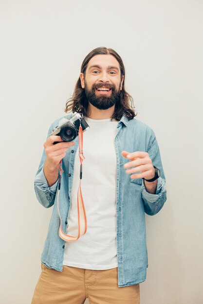 Zachwycony, utalentowany fotograf w zwykłych ubraniach, stojący na tle białej ściany