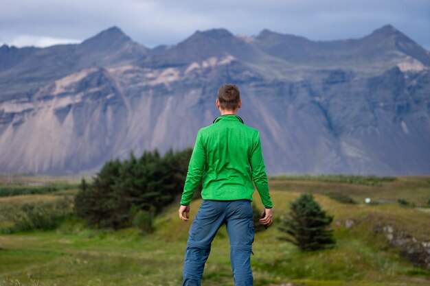 Zad wysoki kaukaski mężczyzna ubrany w zieloną kurtkę stojący na tle góry i mgły. Promowanie zdrowego stylu życia.