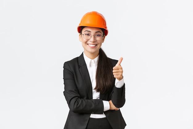 Zadowolona azjatycka przedsiębiorczyni kontroluje przedsiębiorstwo, jest zadowolona z prac budowlanych, pokazuje kciuki w górę z aprobatą, uśmiecha się zachwycona, mówi dobrze zrobione, dobra robota, gwarantuje ukończenie budowy na czas