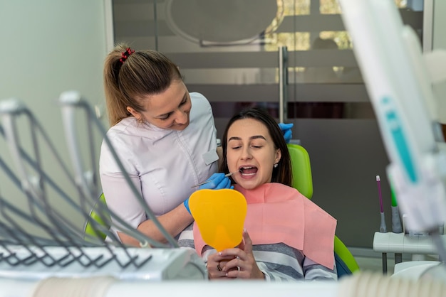 Zadowolona kaukaska kobieta z lekarzem dentystą patrząca w lustro po leczeniu w klinice Wysokiej jakości usługi stomatologiczne