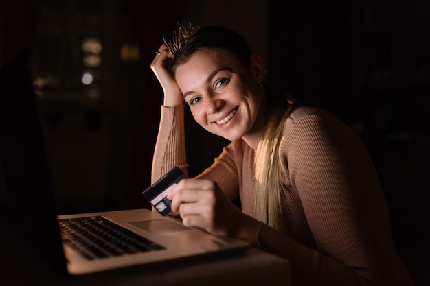 Zadowolona kobieta kupująca online, patrząca na kamerę siedzącą na kolanach