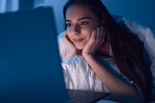 Zadowolona kobieta ogląda film na laptopie w nocy