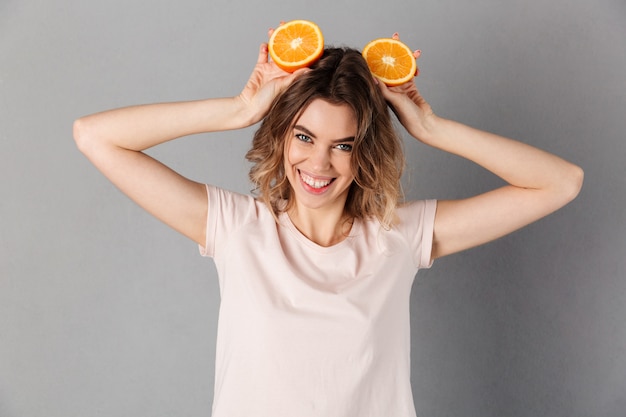 Zadowolona kobieta w koszulce dobrze się bawi i bawi się pomarańczami w szarej sukience