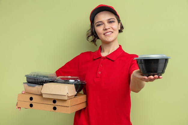 Zadowolona młoda ładna kobieta dostawy trzymająca pojemnik na żywność i opakowanie na pudełkach po pizzy