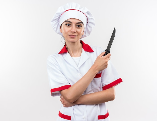 Zadowolona młoda piękna kobieta w mundurze szefa kuchni trzymająca nóż na białej ścianie
