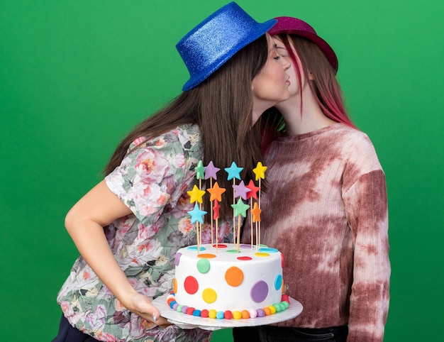 Zadowolone dziewczyny w imprezowych czapkach trzymające ciasto przytulały się nawzajem