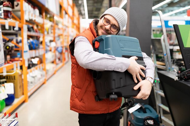 Zadowolony klient przytulający odkurzacz budowlany w hipermarkecie budowlanym