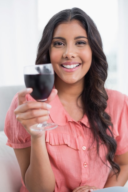 Zadowolony ładny brunetka siedzi na kanapie, trzymając kieliszek do wina