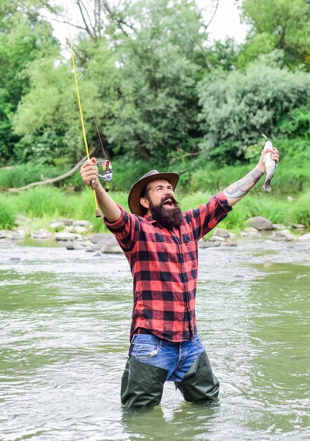 Zadowolony rybak Męskie hobby Fisher Wędkarstwo wymaga uważności i pełnej obecności w chwili Sprzęt wędkarski Fisher Ryba na haczyku Brutalny mężczyzna w gumowych butach stoi w wodzie rzeki