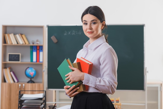 zadowolony z posiadania książek młody nauczyciel stojący przed tablicą w klasie