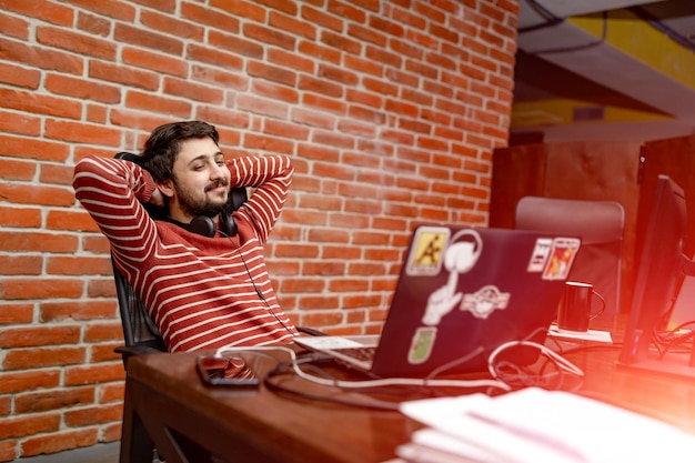 Zadowolony z wykonanej pracy Szczęśliwy młody człowiek pracuje na laptopie siedząc w swoim miejscu pracy w biurze