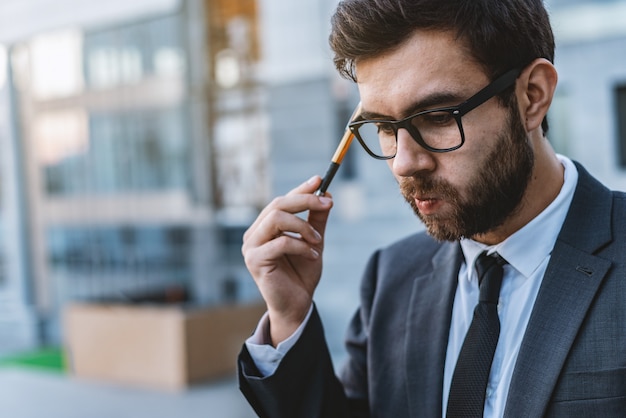 Zadumany Medytacyjny Młody Biznesmen W Eyeglasses Trzyma Pióro W Jego Ręce