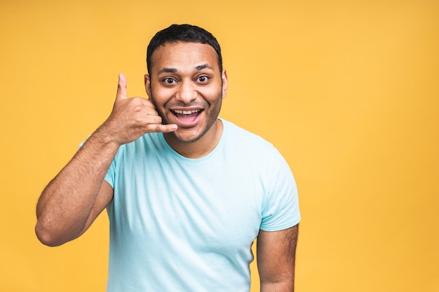 Zadzwoń do mnie znak. Portret szczęśliwy african american indian czarny człowiek rozmawia przez telefon komórkowy na białym tle nad żółtym tle.