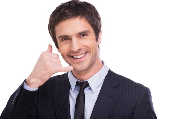 Zadzwoń! Szczęśliwy młody człowiek w koszuli i krawacie gestykuluje telefonem komórkowym w pobliżu twarzy i uśmiecha się