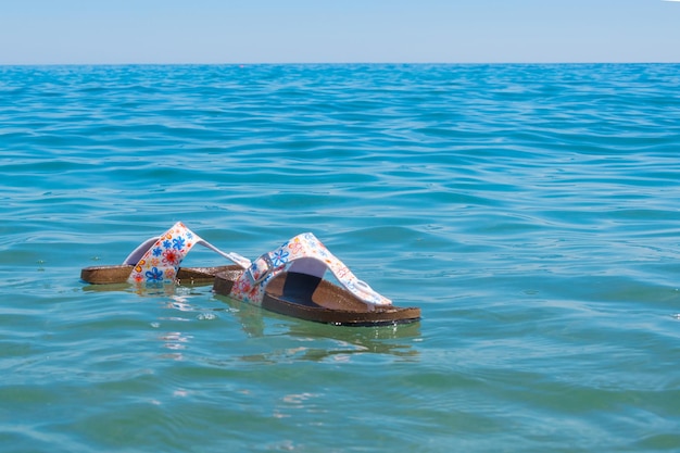 Zaginęły w oceanie nad morzem Klapki damskie Zgubione buty na wakacjach Koncepcja końca wakacji z rozstaniem z morzem