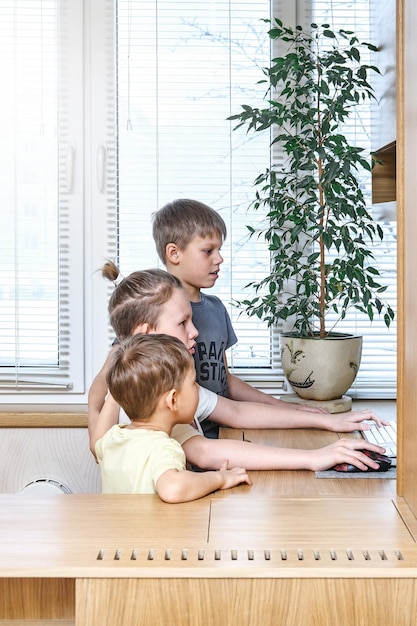 Zainteresowani uczniowie zaglądają do wyświetlacza komputera przy drewnianym biurku z rośliną doniczkową