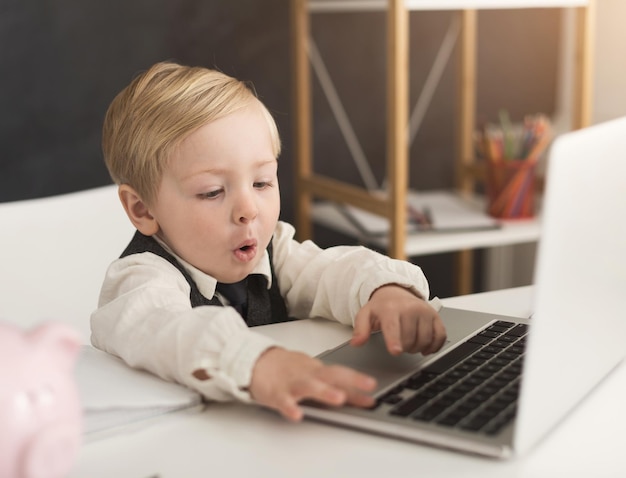 Zainteresowany Mały Biznesmen Pracujący Na Laptopie W Biurze. Chłopiec W Stroju Wizytowym Udający Przystojnego Pracownika