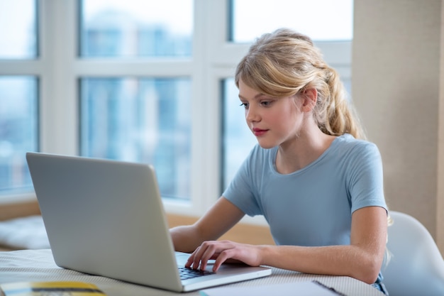 Zajęty. Ładna blondynka siedzi przy laptopie i wygląda na zaangażowaną