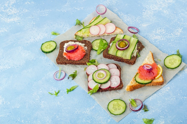 Zakąska, otwarta kanapka z różnymi dodatkami: łosoś i warzywa na papierze na niebieskim tle. Tradycyjna włoska lub skandynawska przekąska. Zdrowe odżywianie