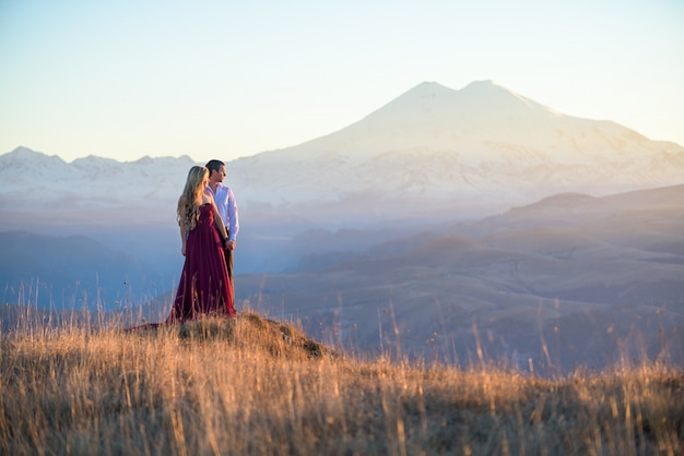 zakochana para obejmuje wycieczkę w góry o zachodzie słońca. dziewczyna w czerwonej sukience o zachodzie słońca