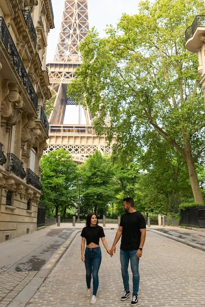 Zakochana para spacerująca ręka w rękę po paryskiej ulicy z wieżą Eiffla za nimi