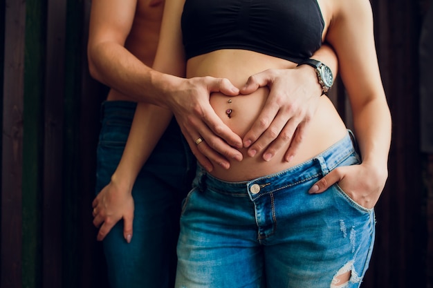 Zakochana para w ciąży stoi przy drewnianej ścianie, śmiejąc się i czekając na swoje dziecko. Oczekiwanie na cud, szczęśliwych rodziców, rodzina.