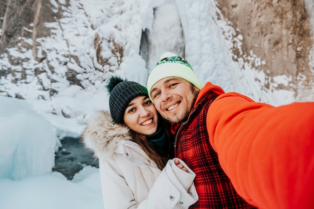 Zdjęcie zakochana para w górach. zakochani robią sobie selfie na tle wodospadu zimą.