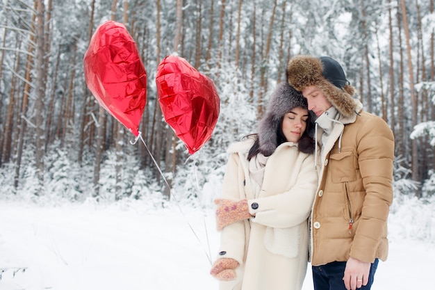 Zakochana para zima. Chłopiec i dziewczynka przytulanie w zimie Śnieg i czarodziejski las z balonami.