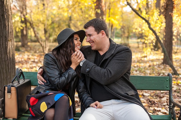 Zakochana szczęśliwa młoda para siedzi na ławce w jesiennym parku