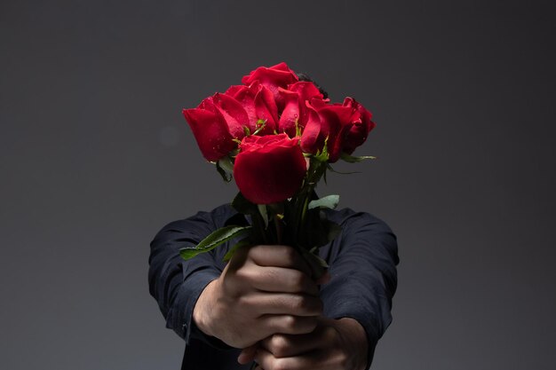zakochany mężczyzna ubrany w ciemne ubrania, trzymający bukiet czerwonych róż zdjęcie w studio szarym tle