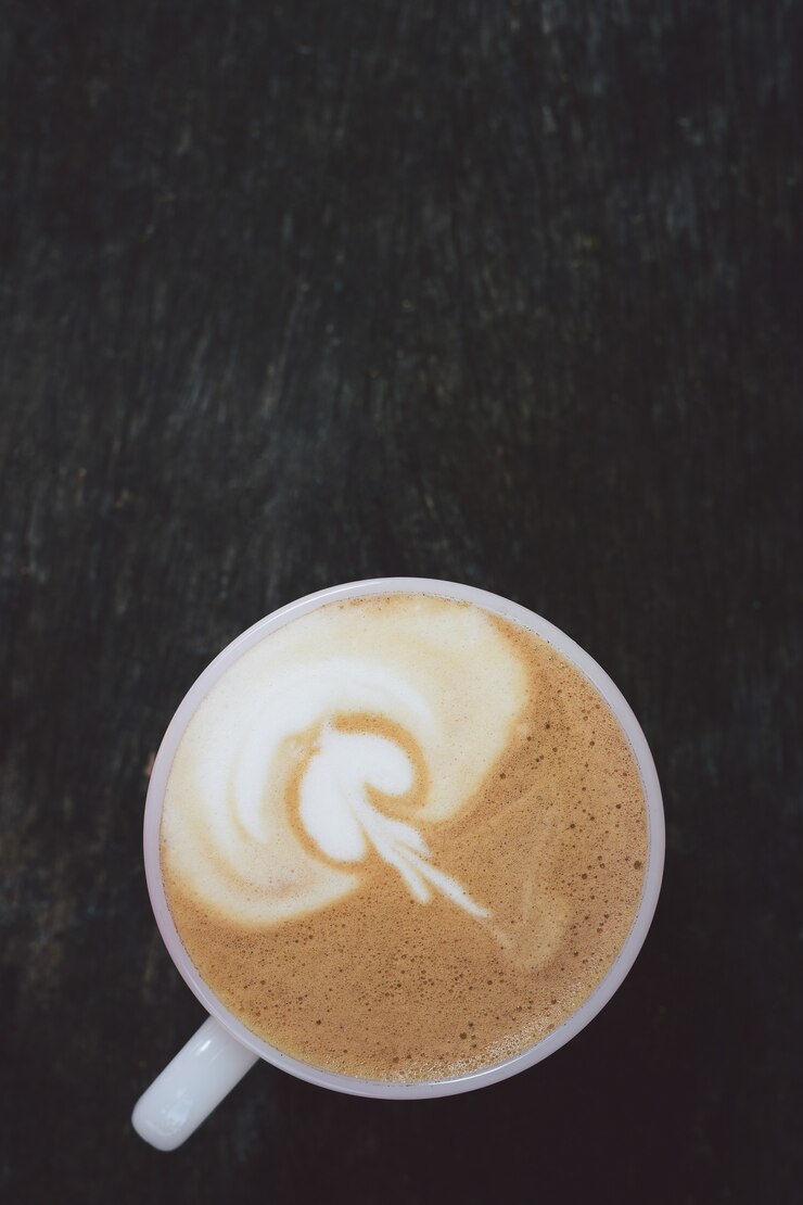 Zakończenie kawowa latte sztuka w filiżance i dojnej pianie above pić na drewnianym stole w ranku.
