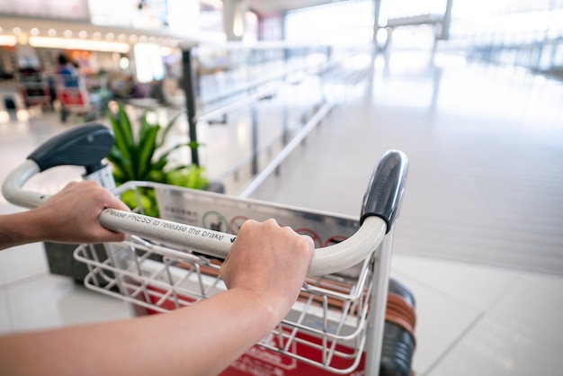 Zdjęcie zakończenie kobiety ręka pcha tramwaj z walizkami przy lotniskiem.