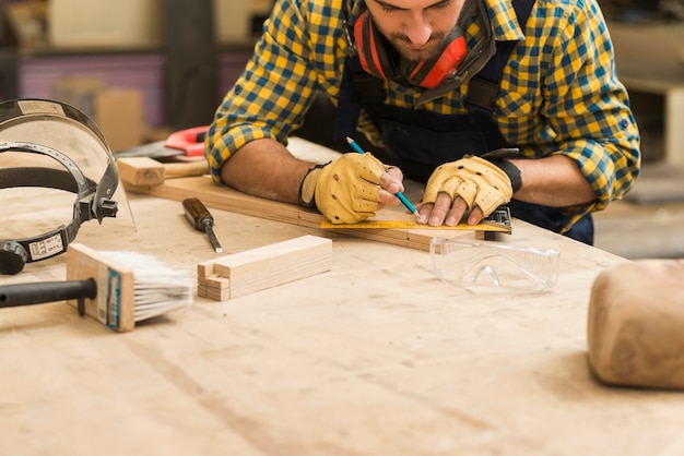 Zdjęcie zakończenie męski cieśla mierzy drewnianego blok z władcą i ołówkiem na drewnianym workbench