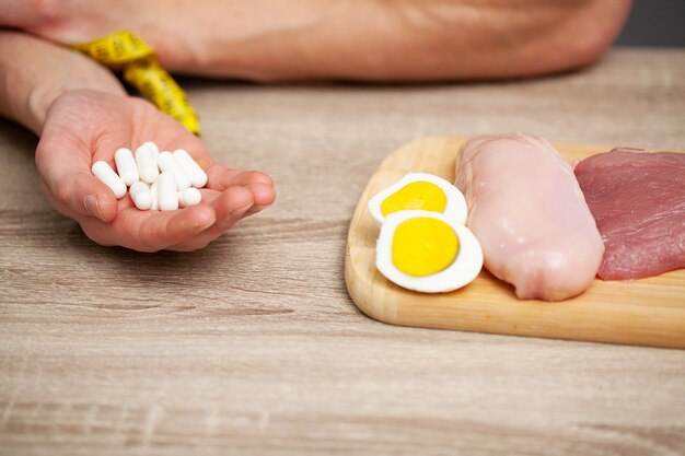 Zakończenie Męskie Ręki Z Jedzeniem Bogatym W Proteinę Na Tnącej Desce I Pigułkę Na Stole.