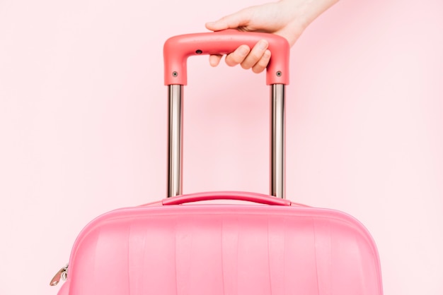 Zdjęcie zakończenie osoby ręki mienia rękojeść podróż bagaż przeciw różowemu tłu