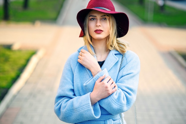 Zdjęcie zakończenie portret młoda piękna uśmiechnięta dziewczyna w błękitnym żakieta i bordowym kapeluszu chodzi w dół ulicę w pogodnym wiosna dniu