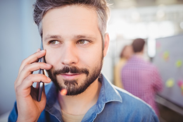 Zakończenie słucha telefon komórkowy przy kreatywnie biurem biznesmen