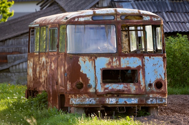 Zakończenie stary opuszczony autobus pasażerski rdzewieje w wysokości zieleni chwastowej trawie na krawędzi zaoranego brązu pola na jaskrawym wiosna dniu pod błękitnym ranku niebem z łamanymi okno.